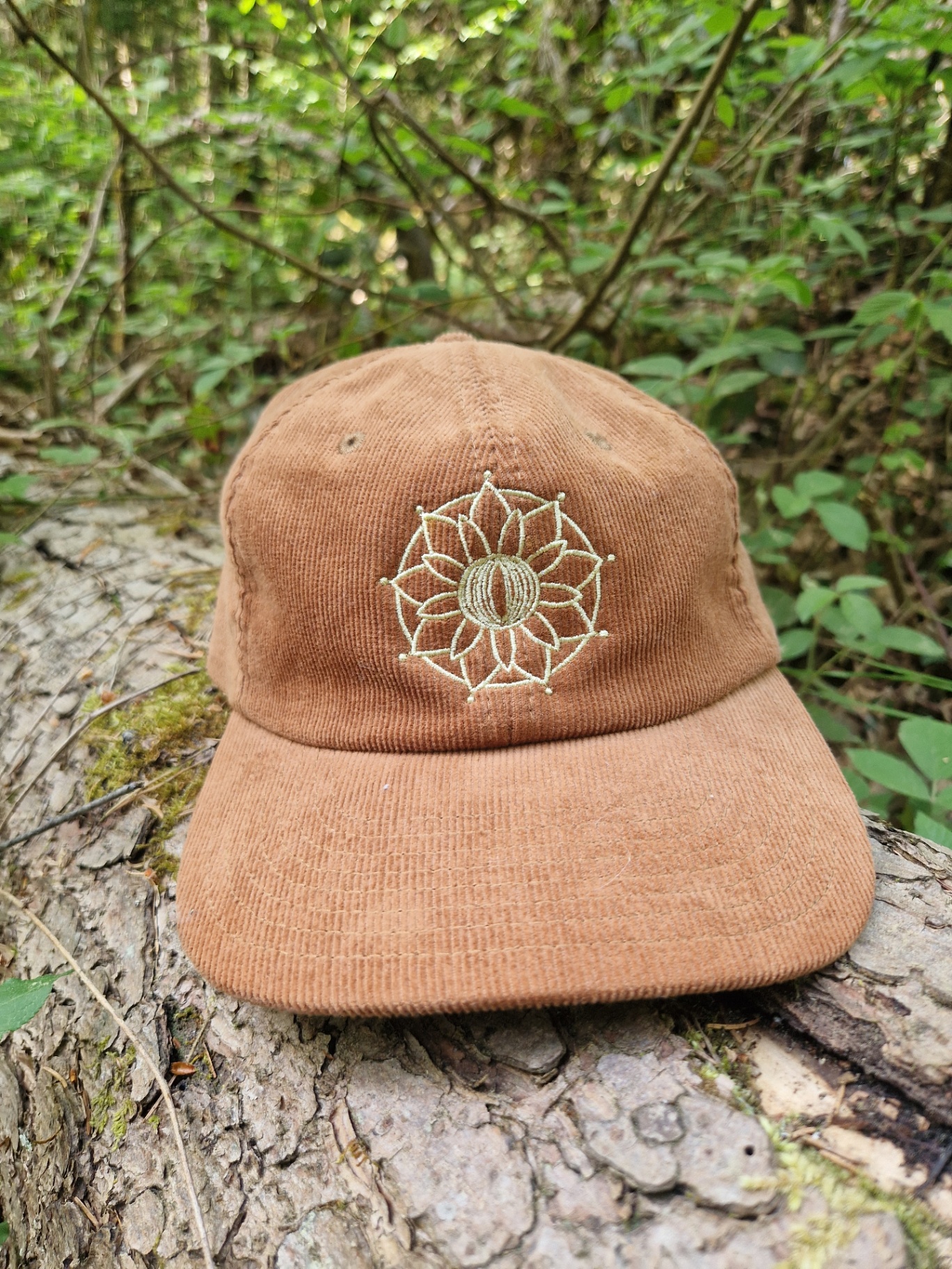 Lockeneule Cord-Cap in Camel mit goldener Mandala-Stickerei auf einem Baumstamm