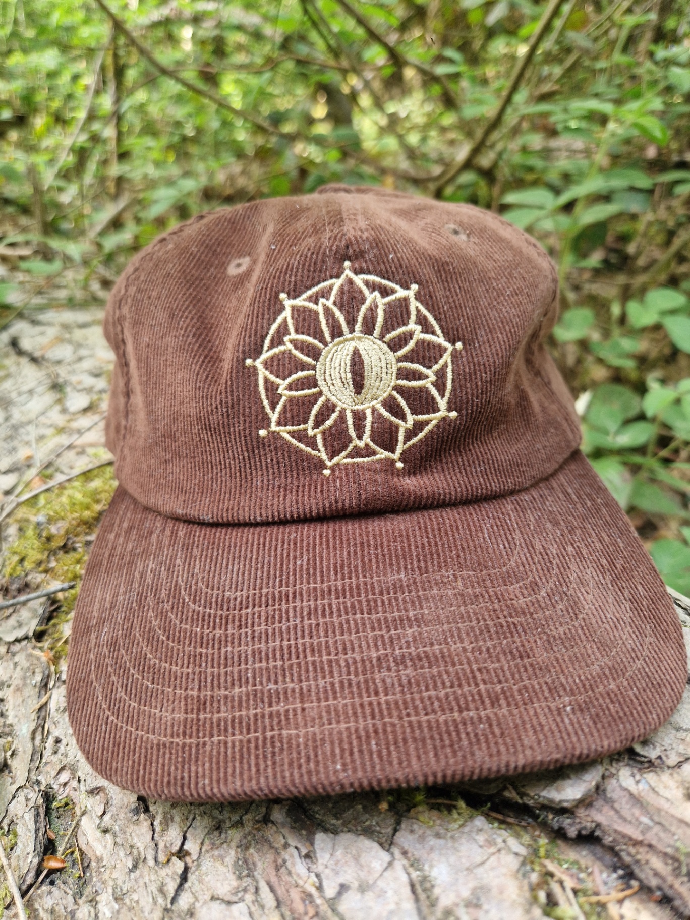 Lockeneule Cord-Cap in Braun mit goldener Mandala-Stickerei auf einem Baumstamm